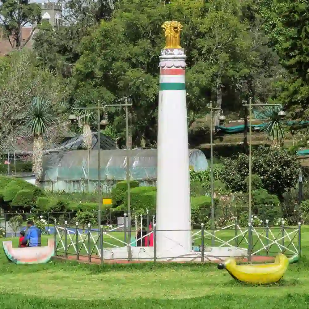 Vibrant flower beds and green lawns at Bryant Park, Kodaikanal, featuring a central statue and tall trees in the back.