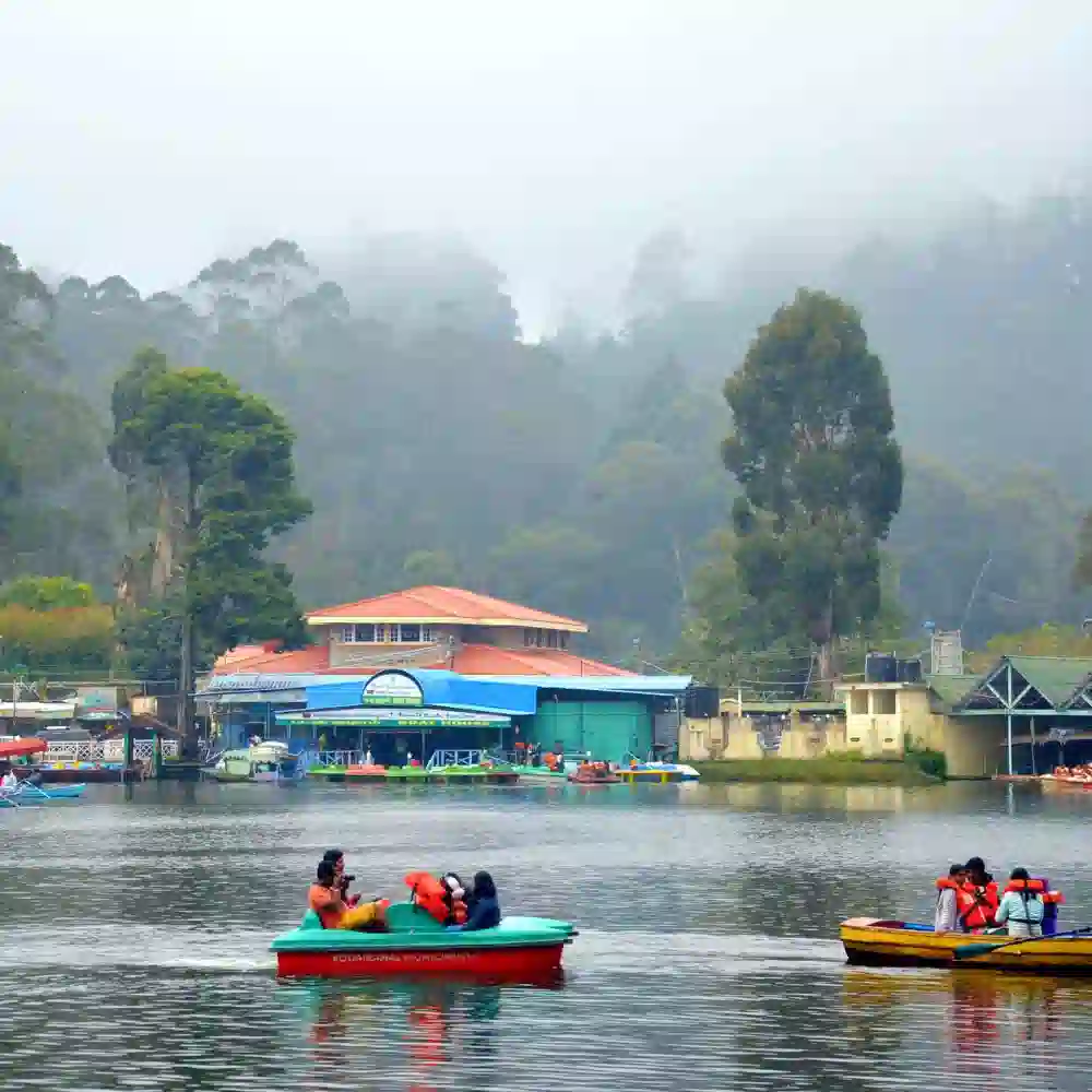 Boating in Kodaikanal Lake with misty hills, colorful paddle boats and the Kodaikanal Municipality boat house building.