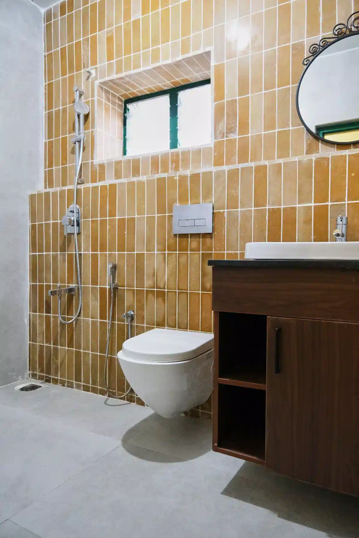 Modern bathroom at Cardamom Pods with mustard yellow wall tiles, wood vanity, round mirror and sleek white fixtures.
